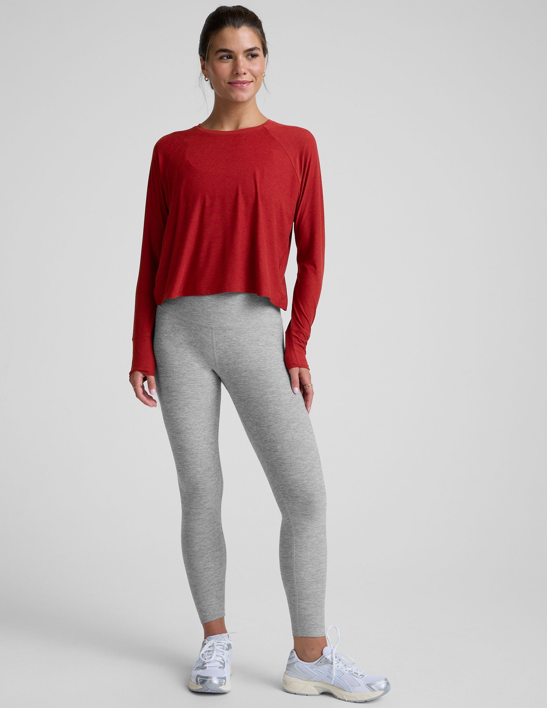 model is wearing a red crewneck long sleeve top and grey leggings against a plain background.