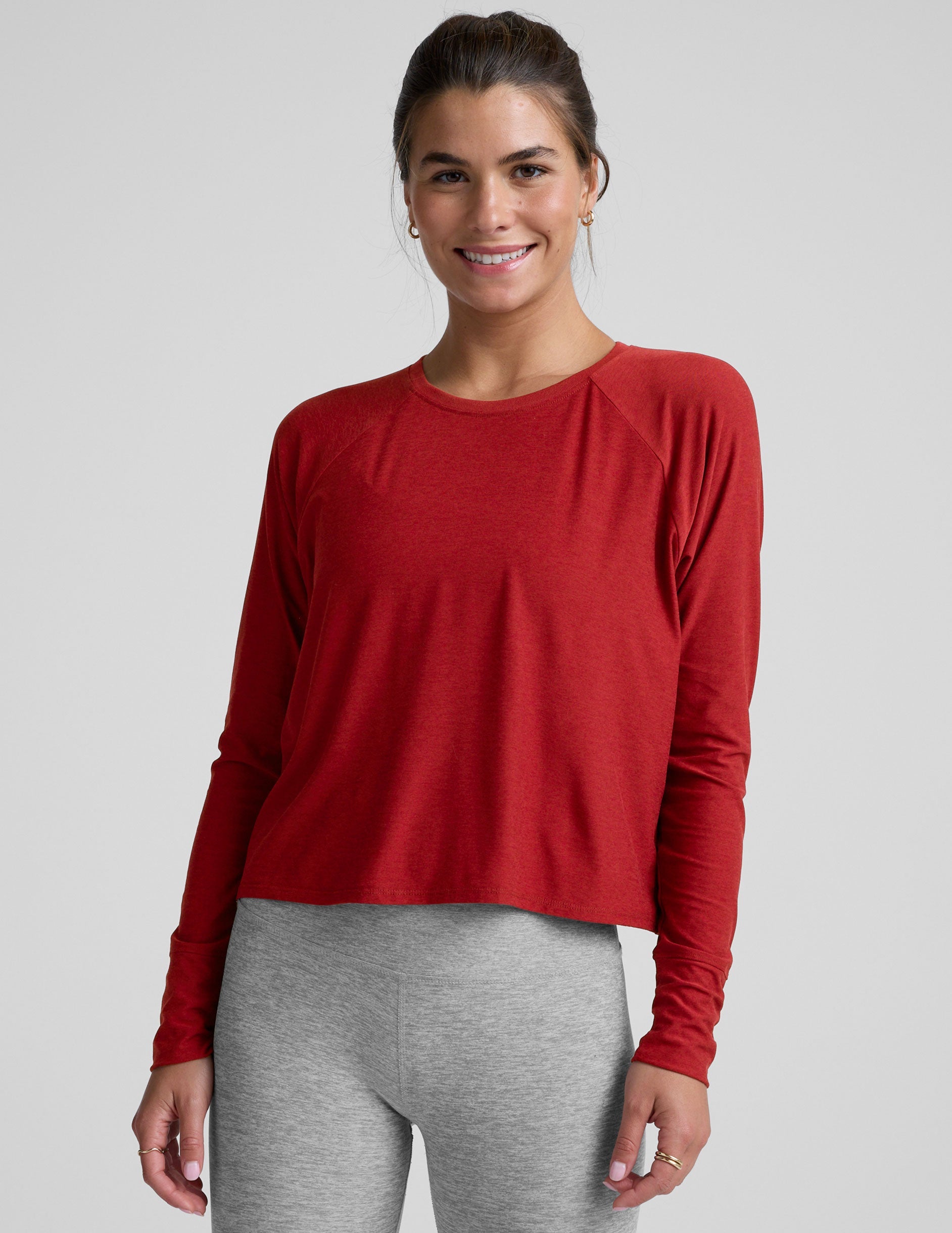 model is wearing a red crewneck long sleeve top and grey leggings against a plain background.