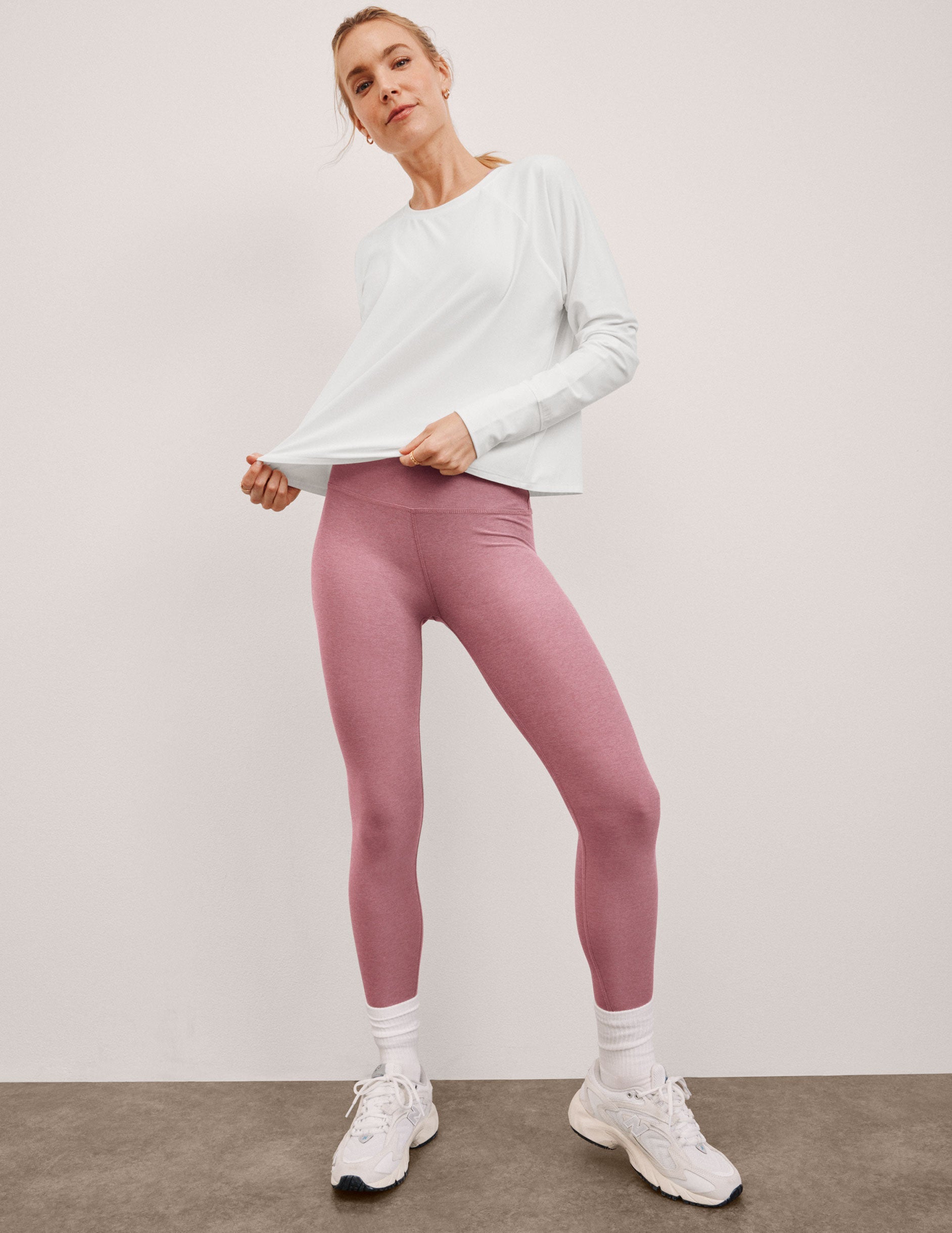 model wearing a white long-sleeve top and pink leggings against a plain background.