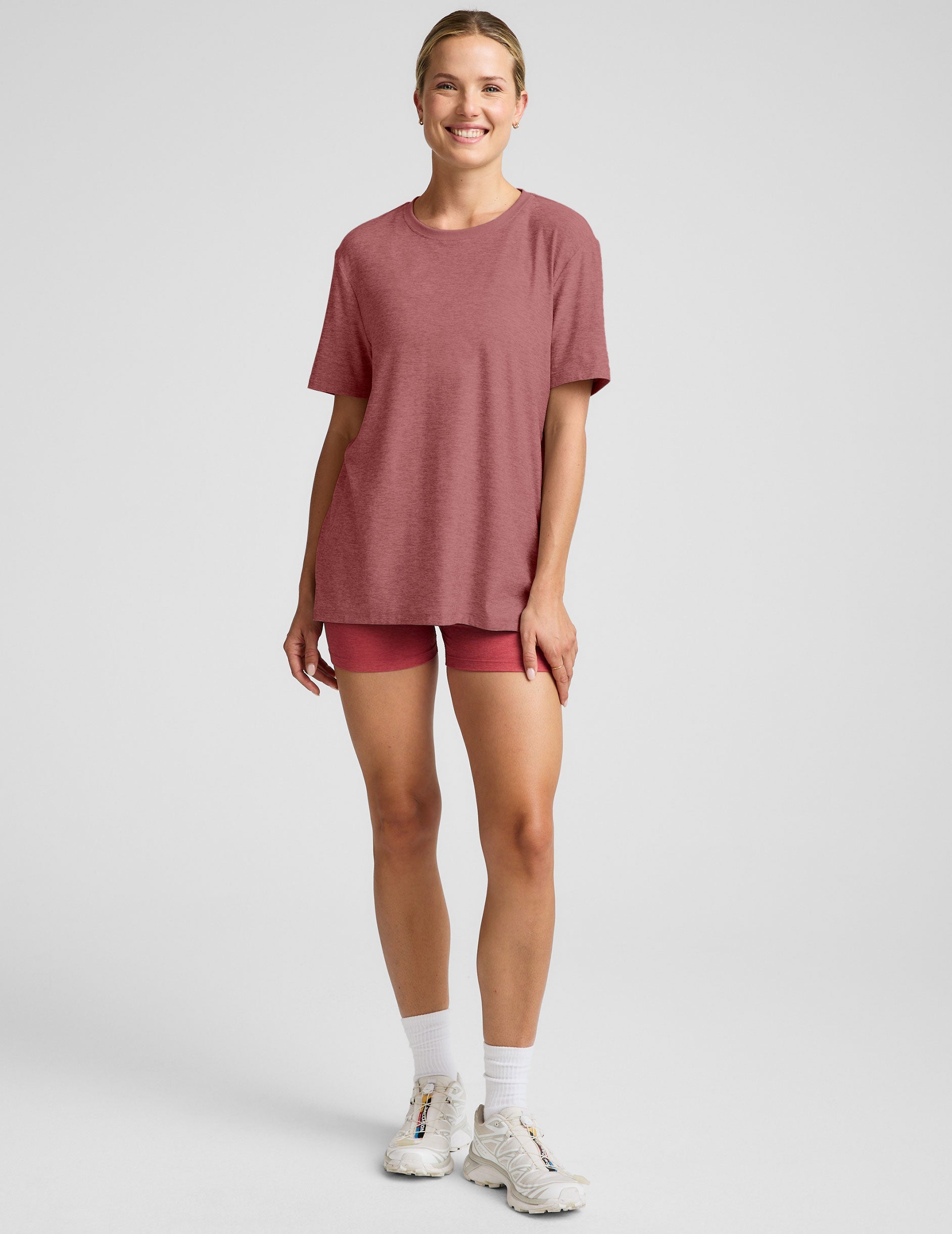 model wearing an oversized men's red t-shirt and shorts on a plain background.