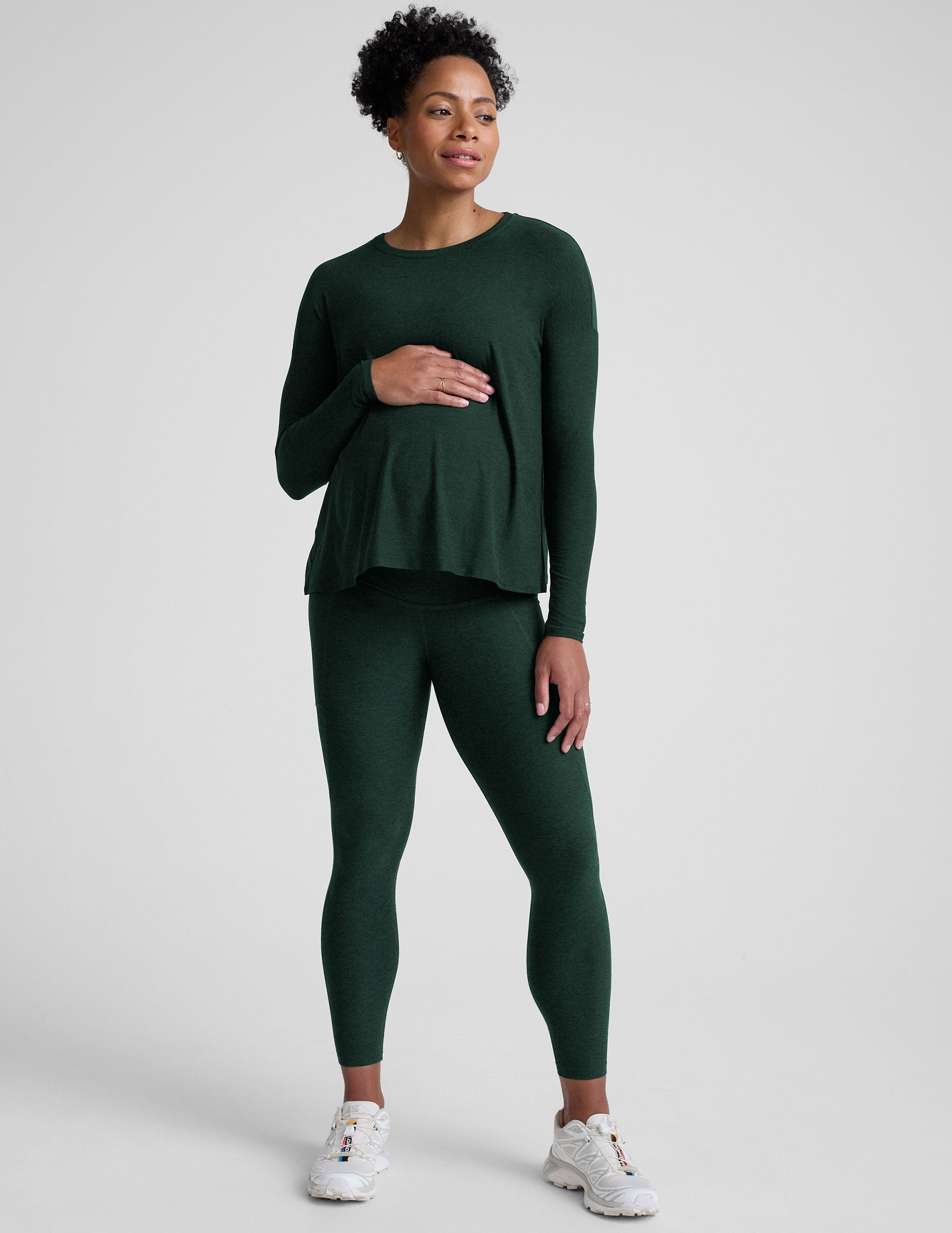 model wearing a green maternity crew neck long-sleeve top and leggings against a light gray background.