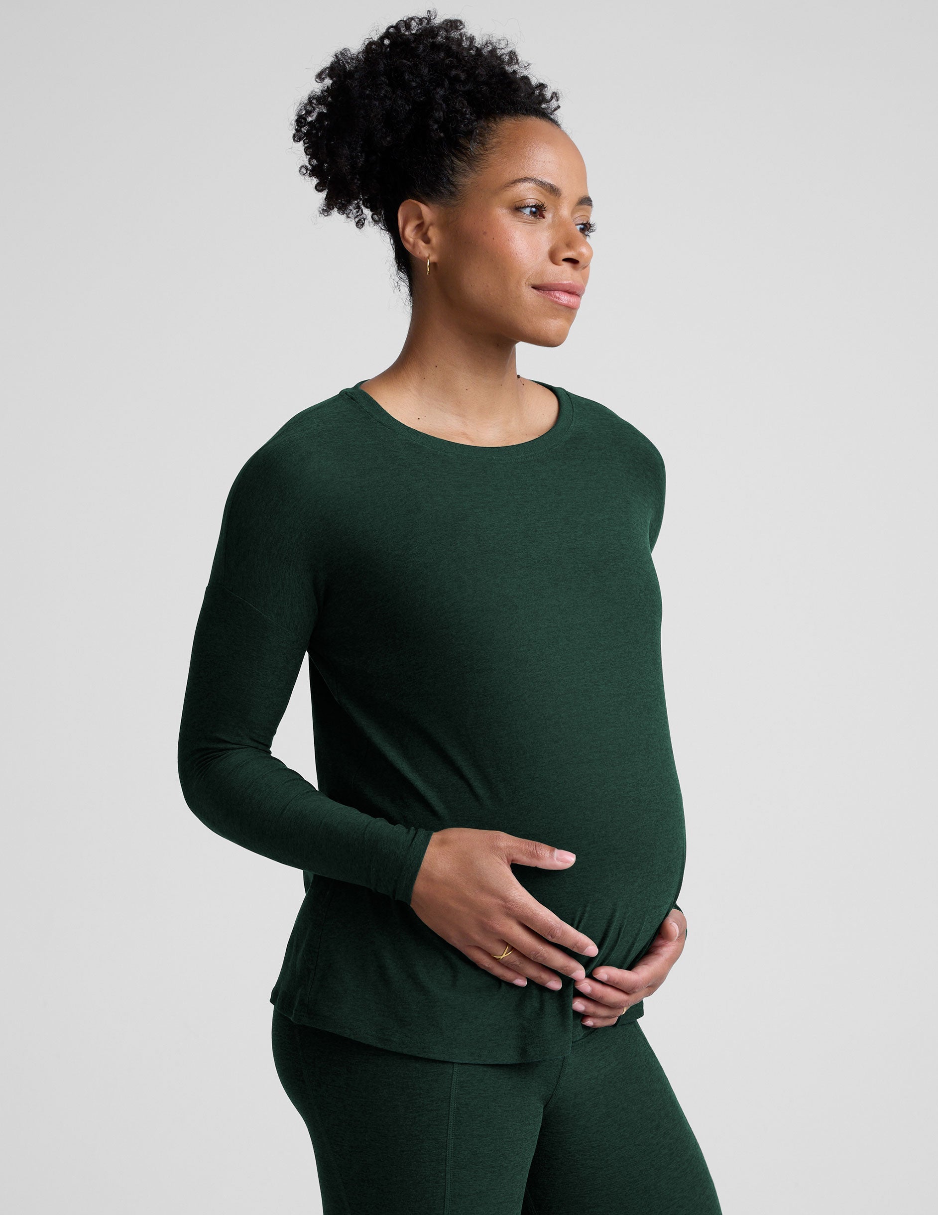 model wearing a green maternity crew neck long-sleeve top and leggings against a light gray background.