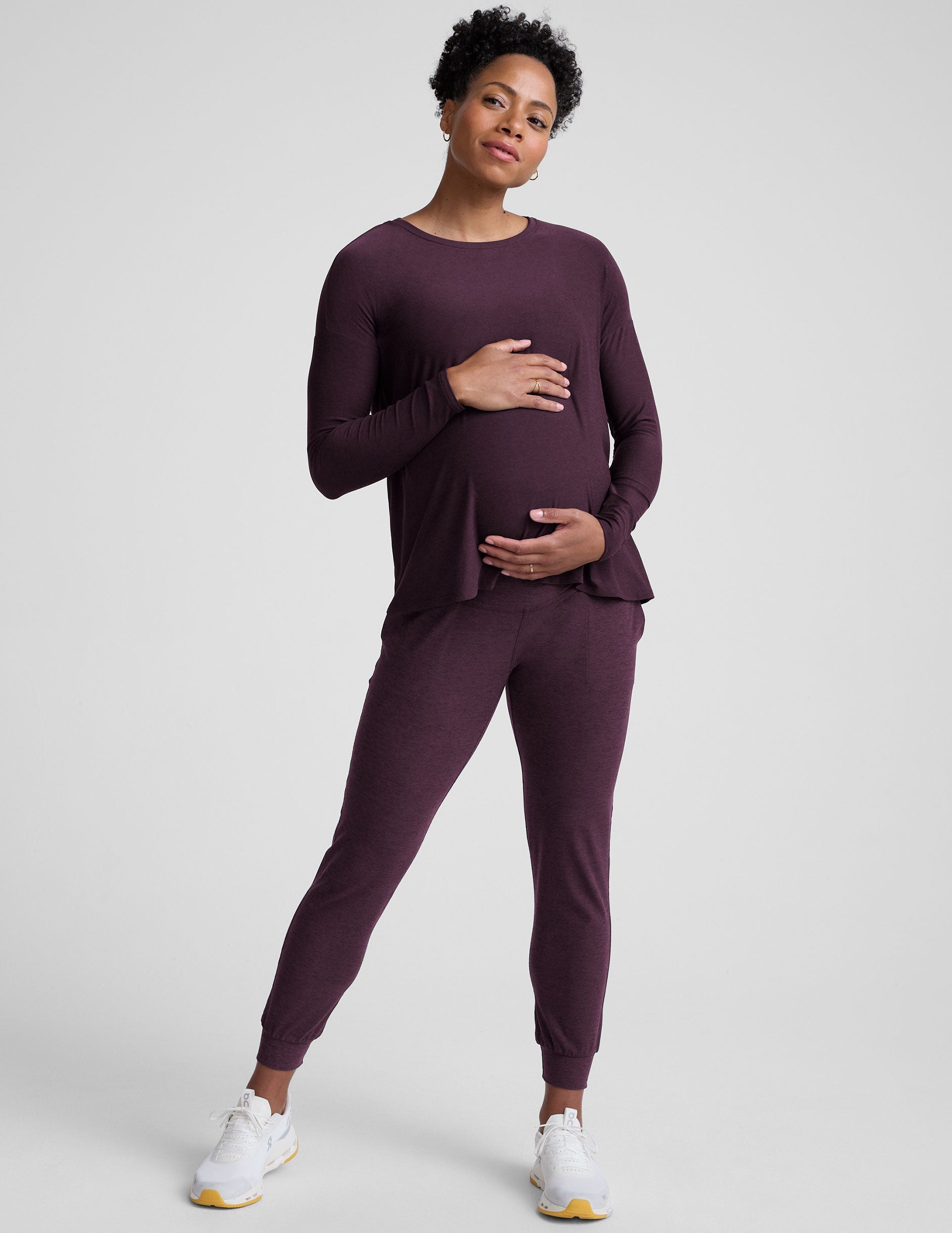 model wearing a purple maternity long sleeve crew neck top and joggers against a light gray background.