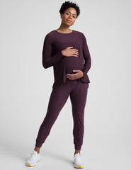 model wearing a purple maternity long sleeve crew neck top and joggers against a light gray background.