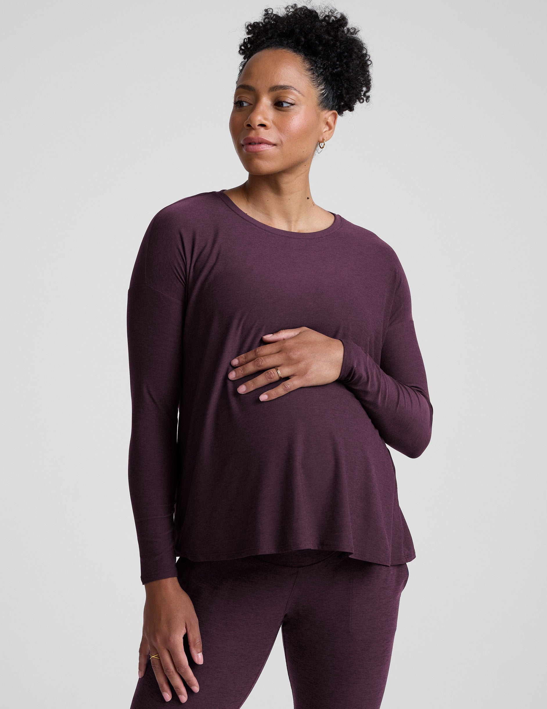 model wearing a purple maternity long sleeve crew neck top and joggers against a light gray background.