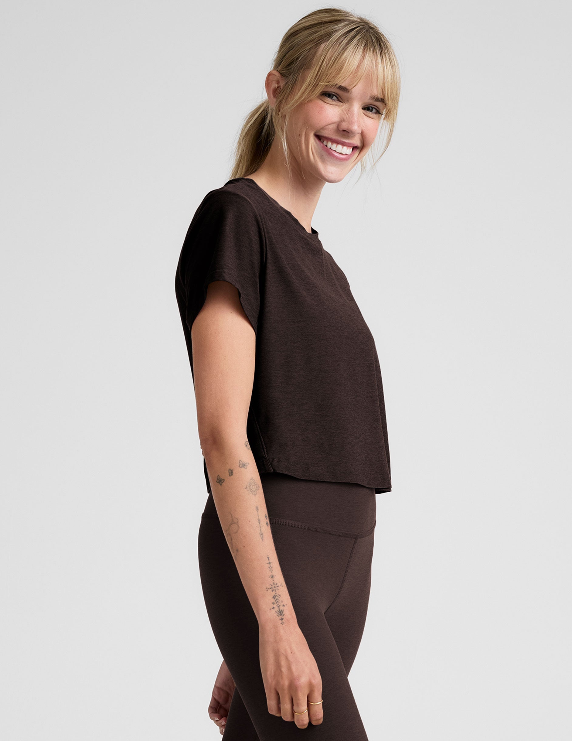 woman wearing a brown cropped t-shirt and leggings on a plain background.