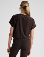 woman wearing a brown cropped t-shirt and leggings on a plain background.