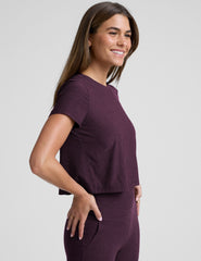 model wearing a purple cropped crew neck t-shirt and pants on a plain background.