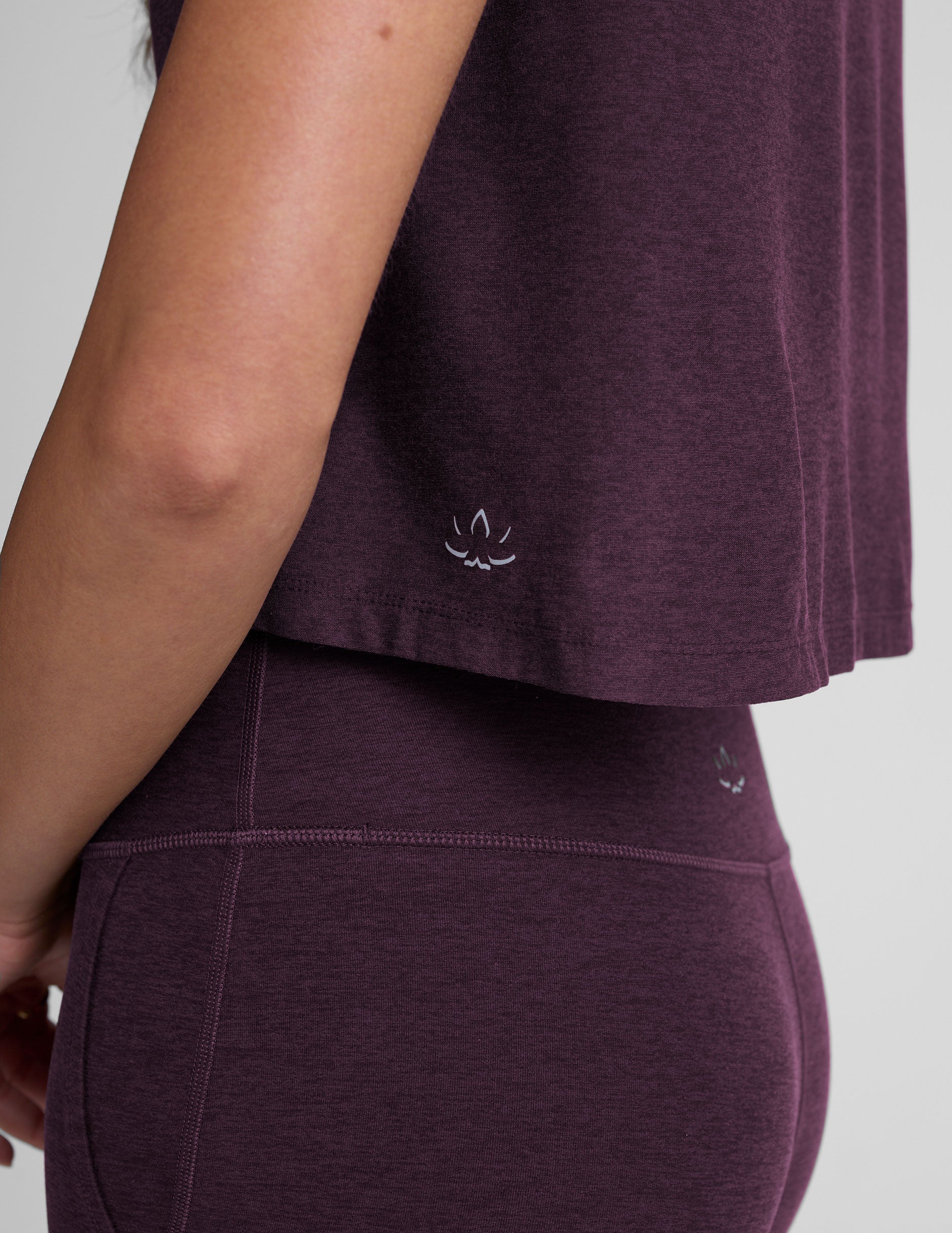 model wearing a purple cropped crew neck t-shirt and pants on a plain background.