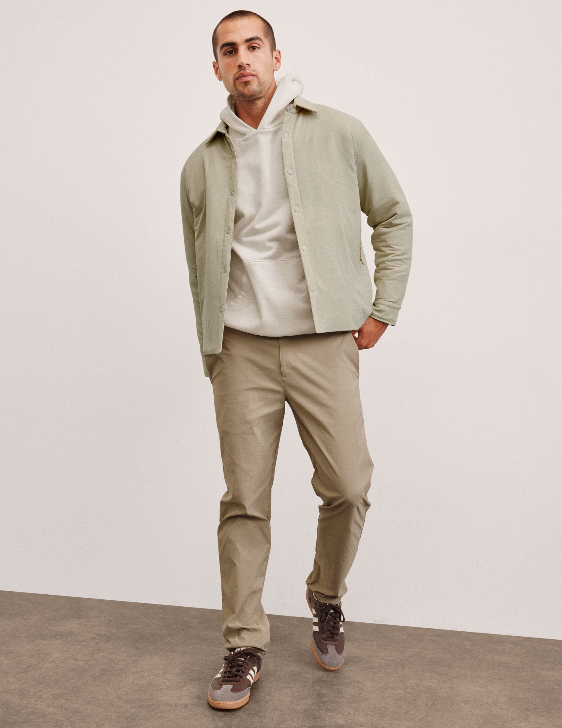 man wearing a light jacket and beige chino pants against a plain background.