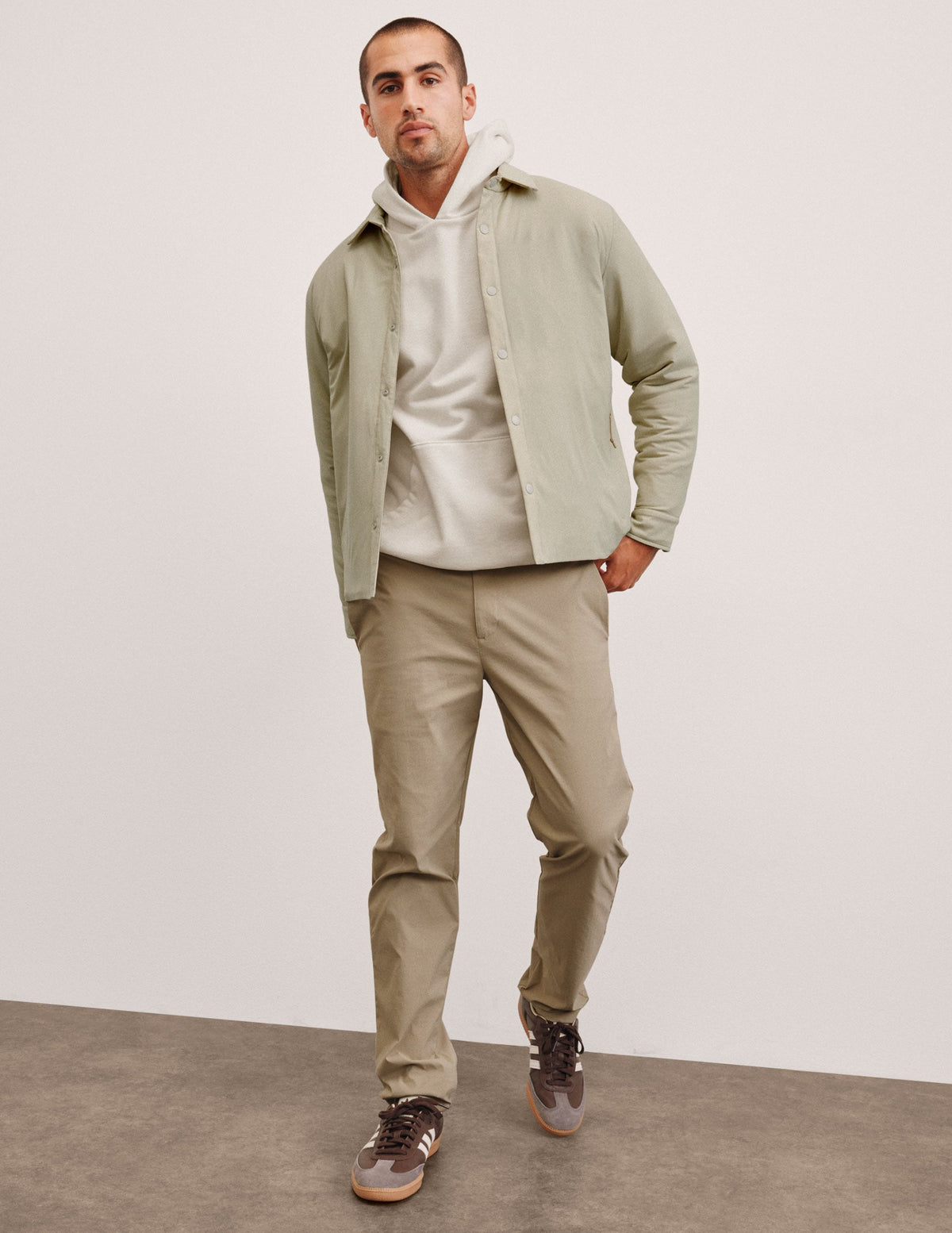 man wearing a light jacket and beige chino pants against a plain background.