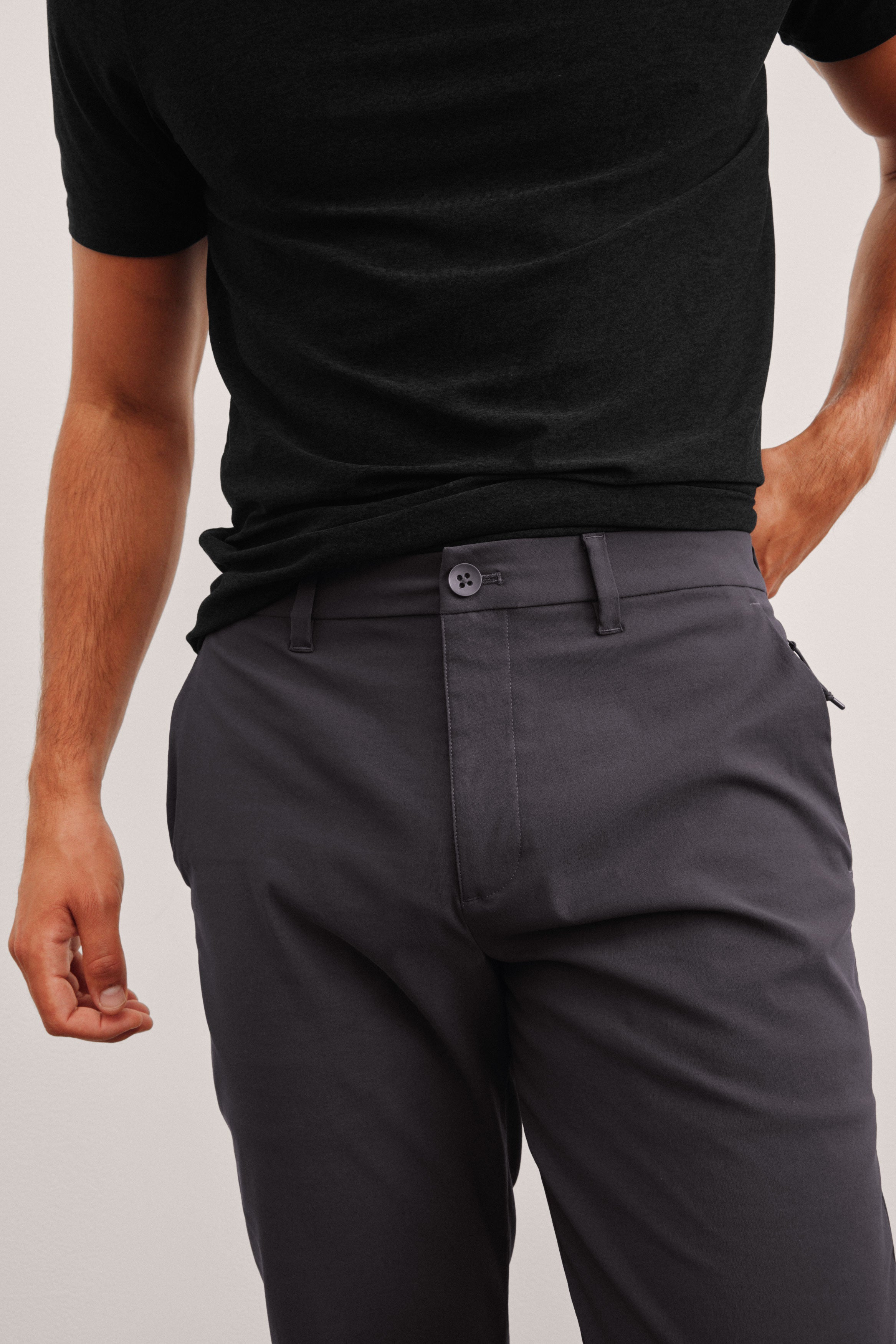 model wearing a black men's t-shirt and gray pants on a plain background.