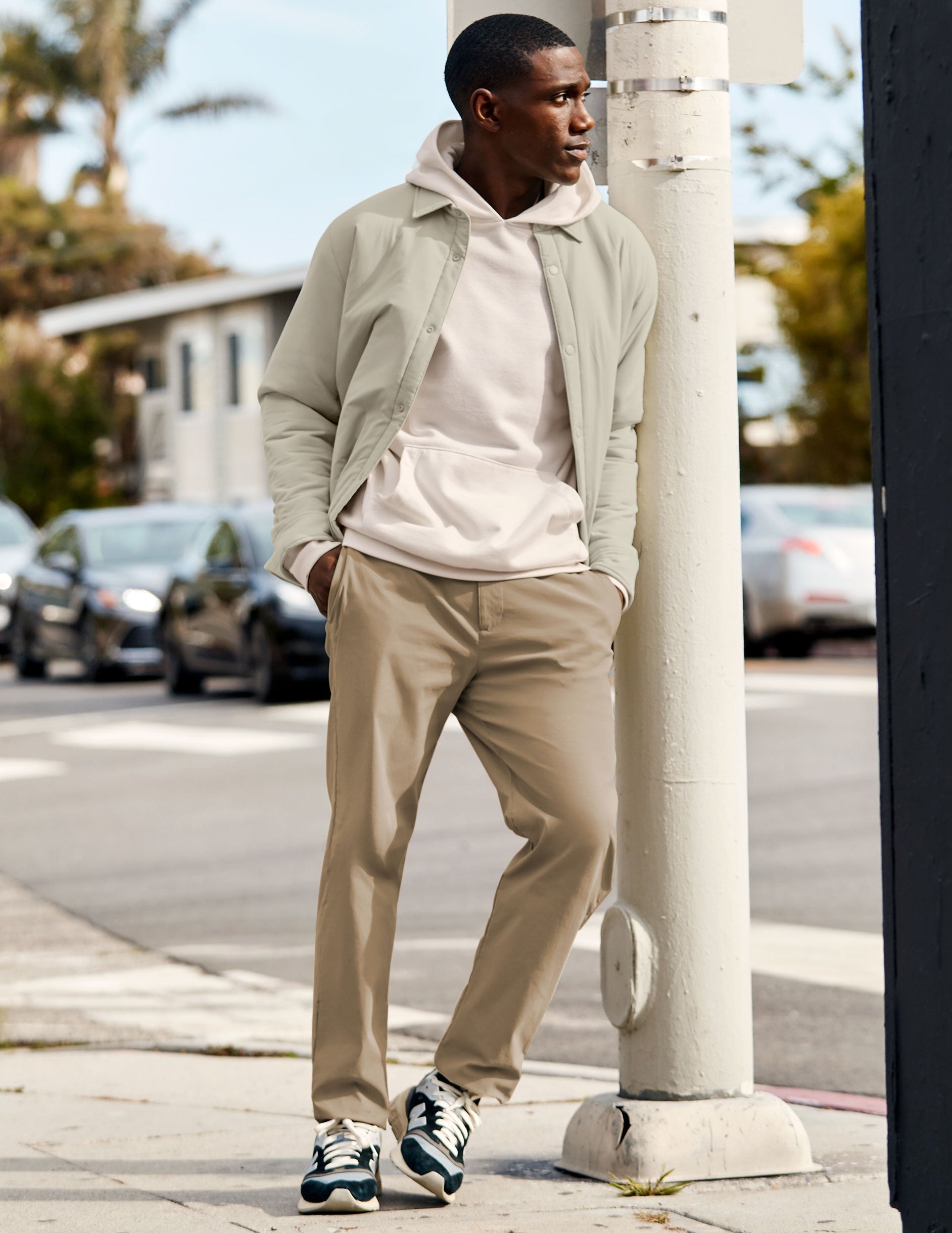 man wearing a white hoodie and beige chino pants standing on a sidewalk.