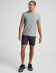 man wearing a grey crew neck t-shirt and black chino shorts with pockets on a plain background.