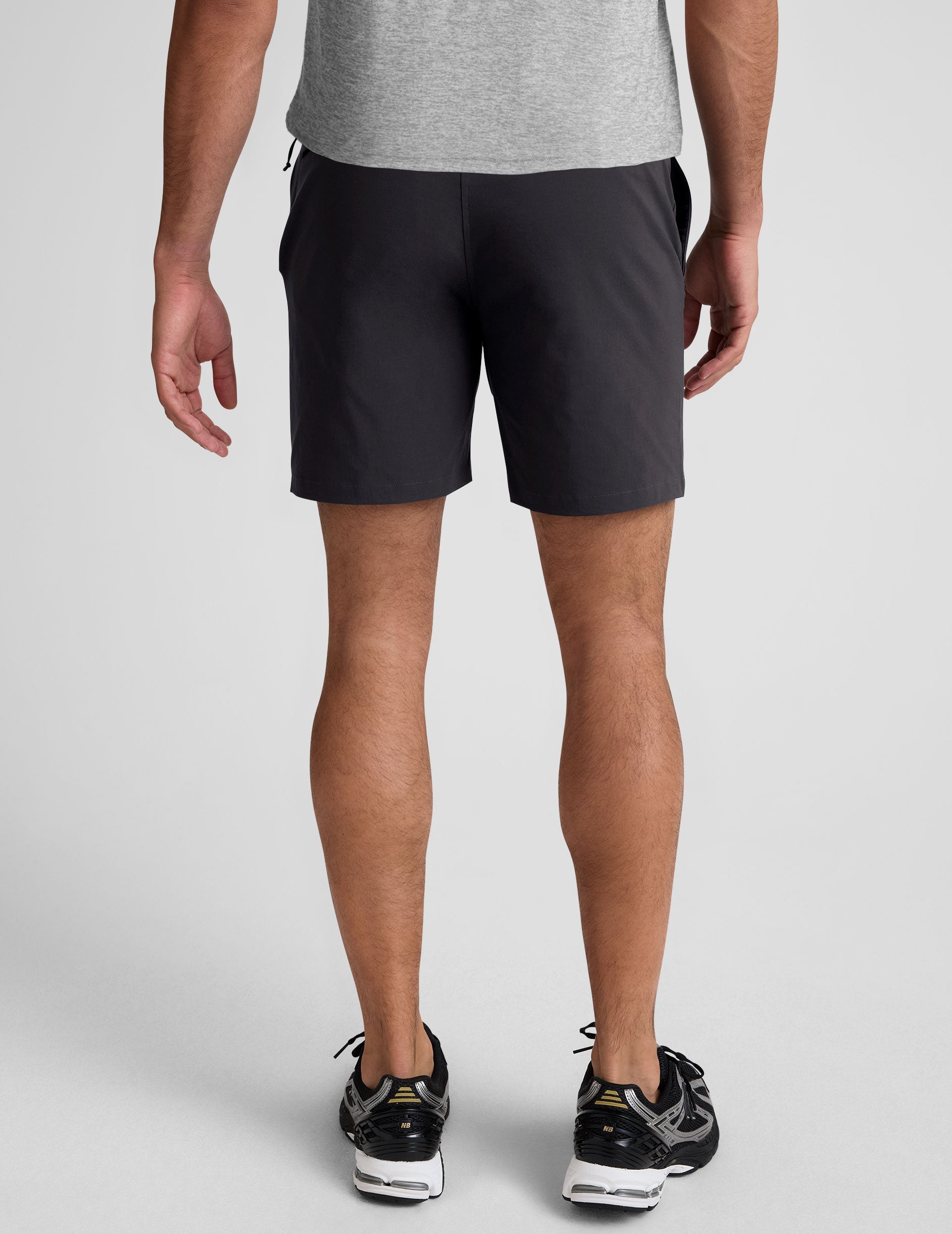 man wearing a grey crew neck t-shirt and black chino shorts with pockets on a plain background.