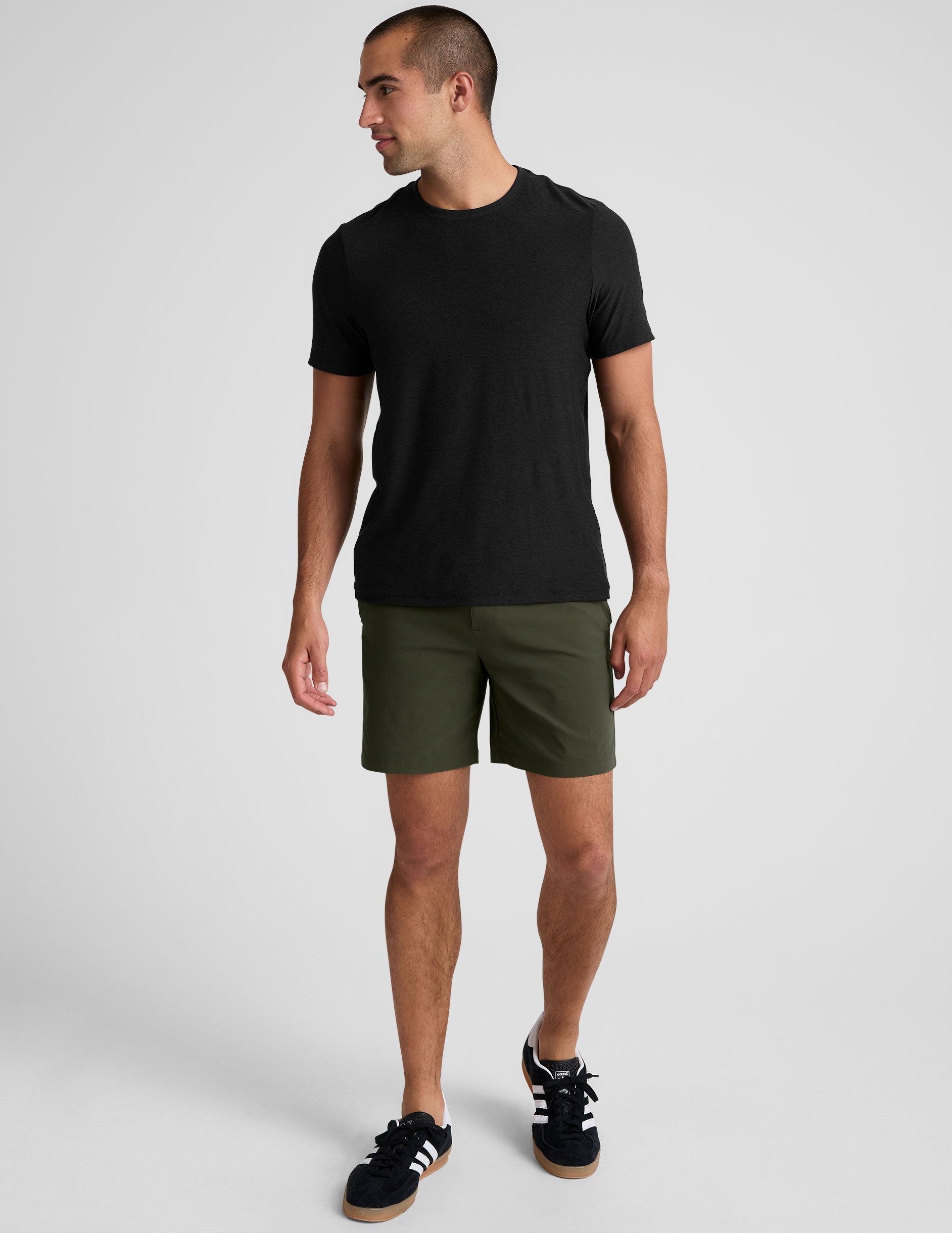 man wearing a black crew neck t-shirt and green chino shorts with pockets on a plain background.