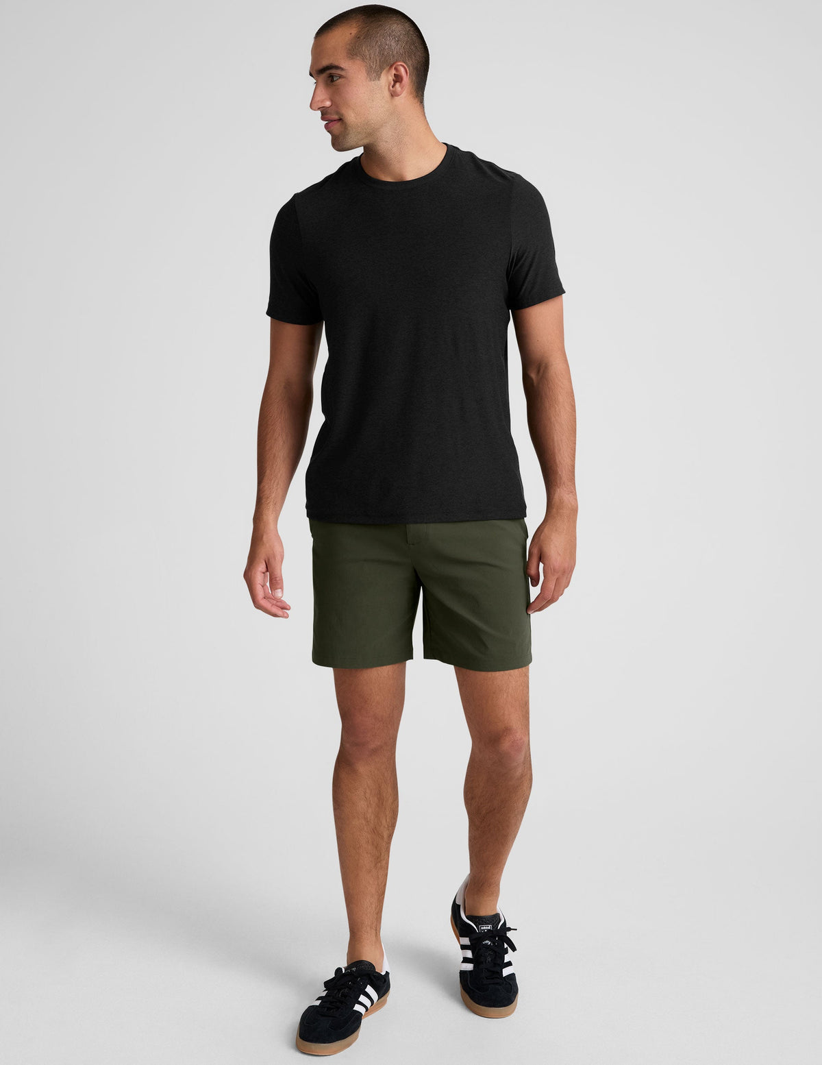 man wearing a black crew neck t-shirt and green chino shorts with pockets on a plain background.