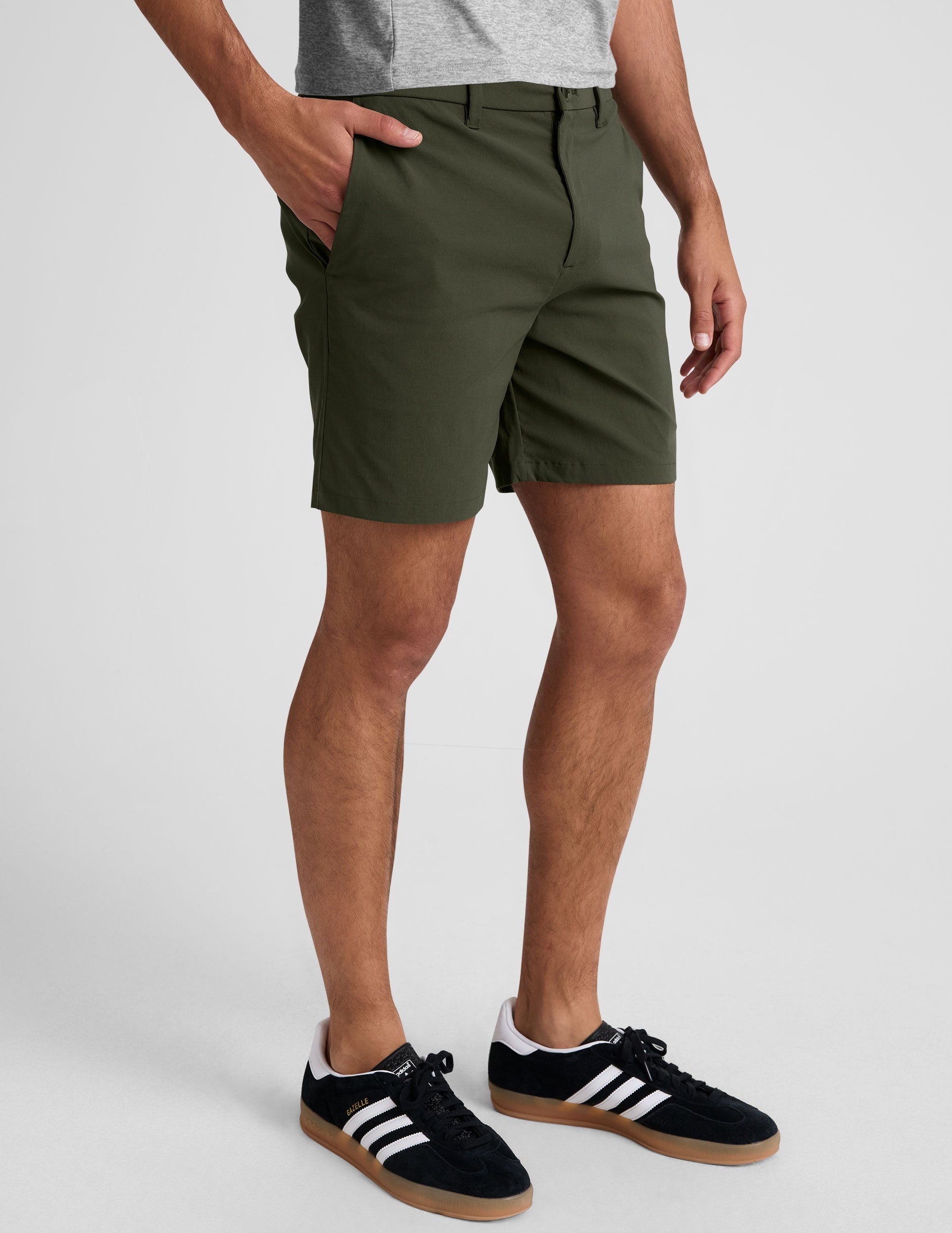 man wearing a grey crew neck t-shirt and green chino shorts with pockets on a plain background.