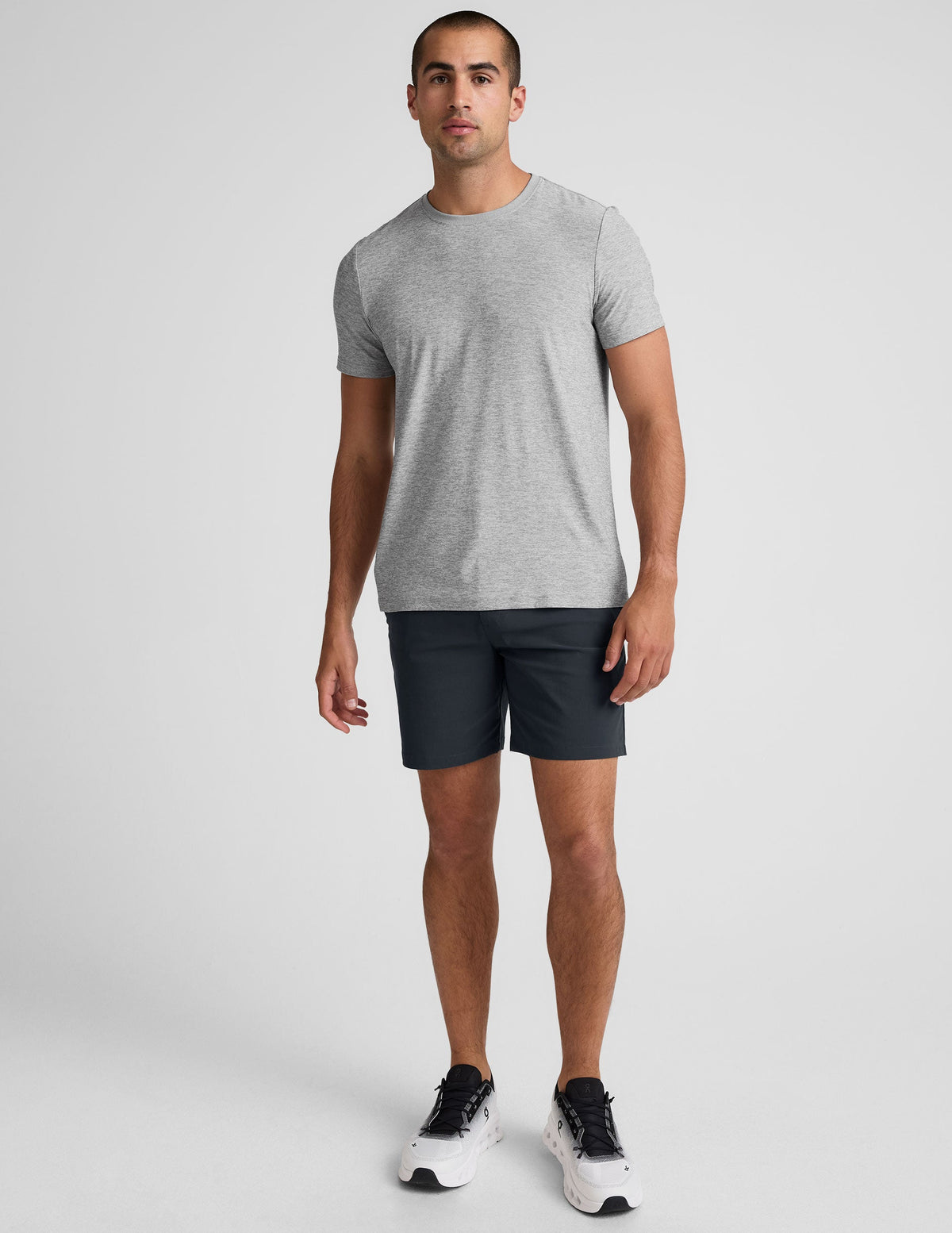 man wearing a gray crew neck t-shirt and blue chino shorts with pockets on a plain background.