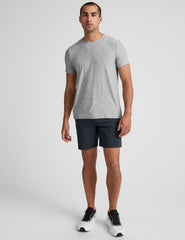man wearing a gray crew neck t-shirt and blue chino shorts with pockets on a plain background.