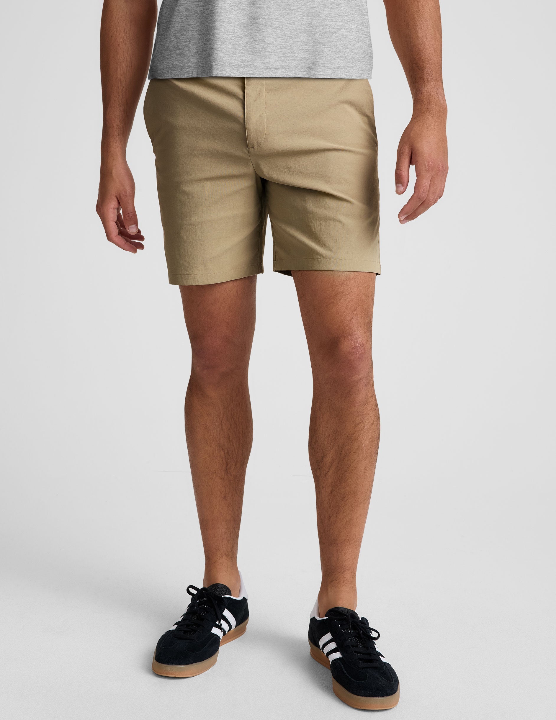 man wearing a grey crew neck t-shirt and beige chino shorts with pockets standing against a plain background.