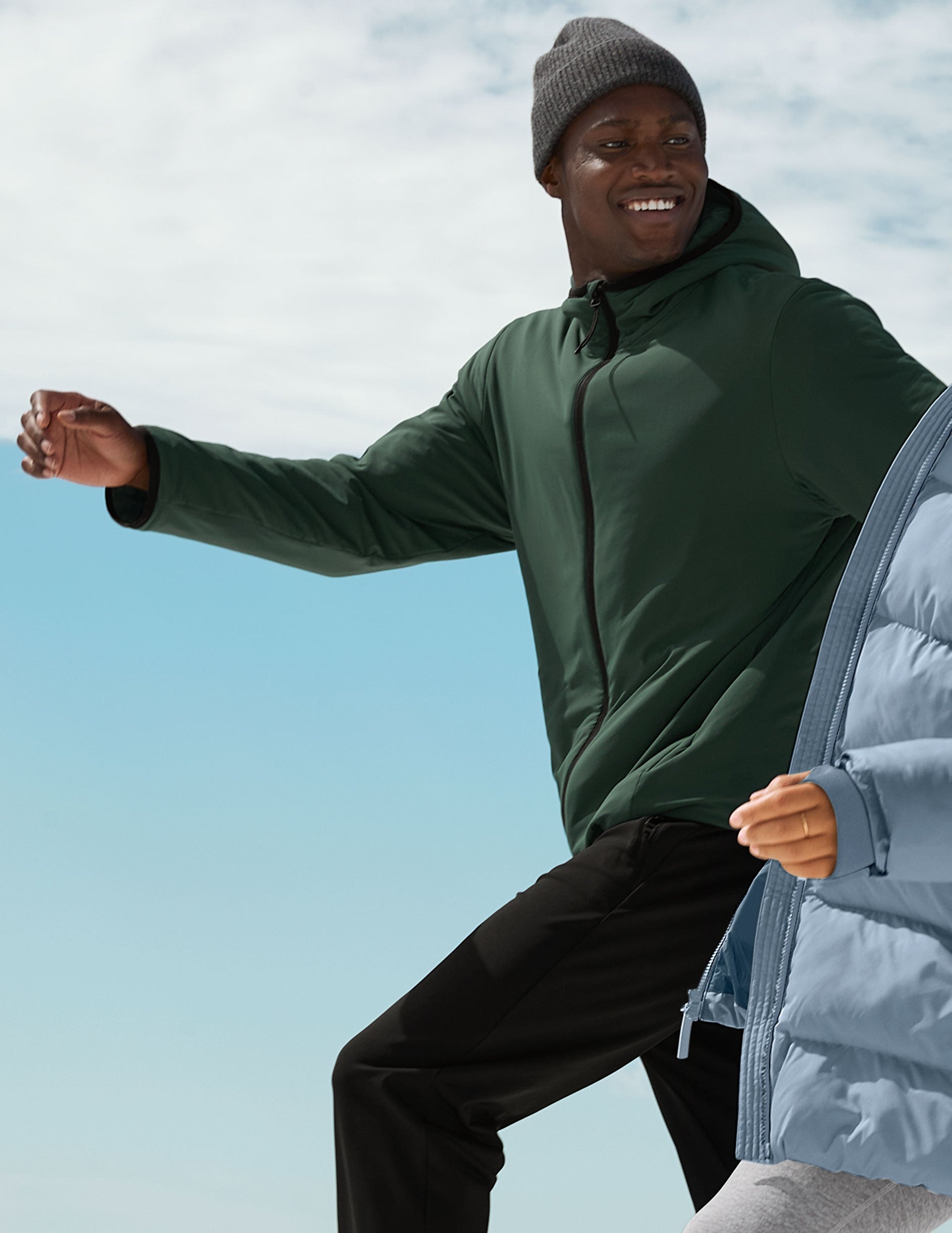 man wearing a green jacket and black pants against a blue sky.