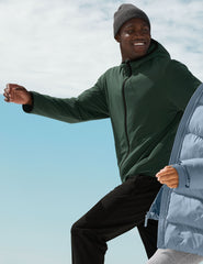man wearing a green jacket and black pants against a blue sky.