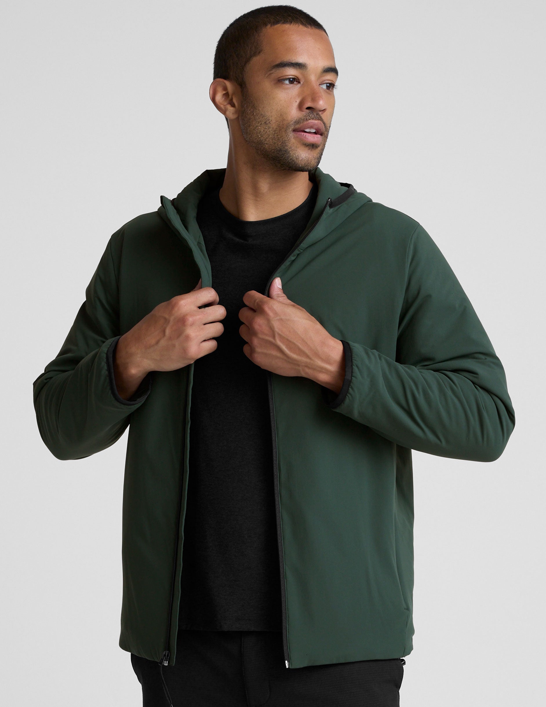 man wearing a green jacket with a hood on a gray background.