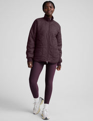 woman wearing a purple quilted jacket against a plain background.