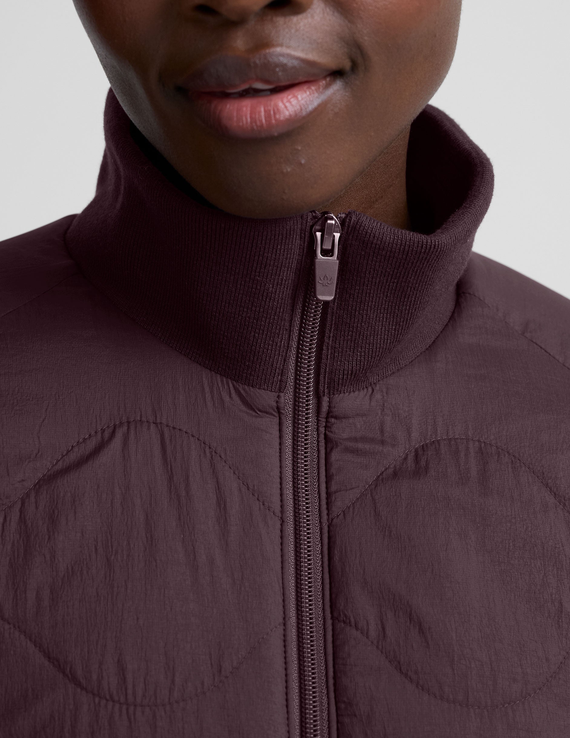 woman wearing a purple quilted jacket against a plain background.