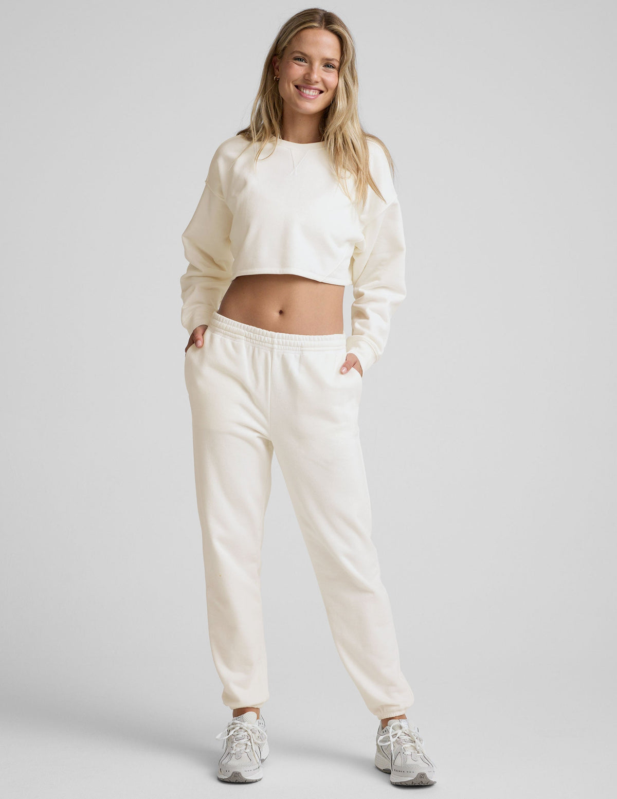 woman wearing a white fleece cropped sweatshirt and white fleece sweatpants against a plain background.