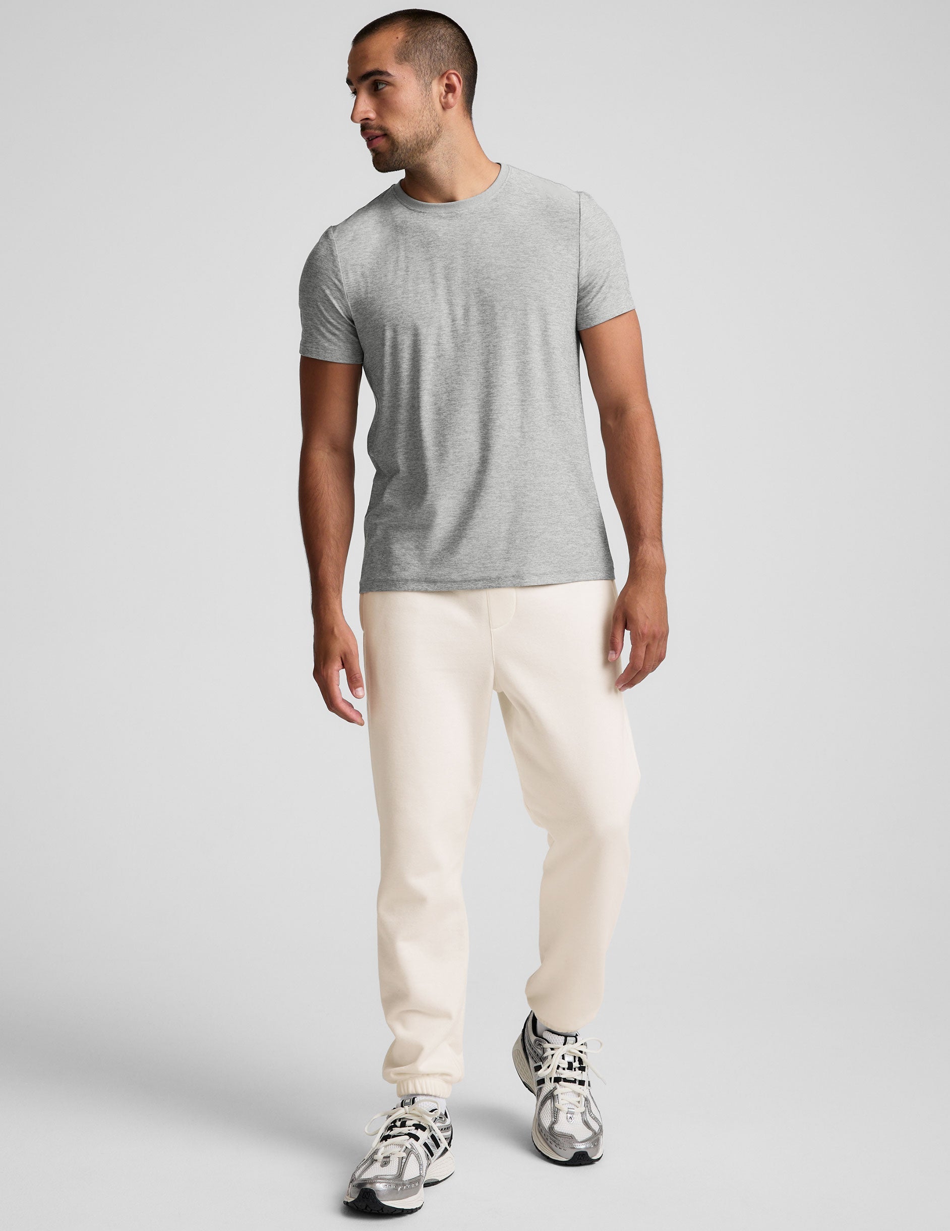 man wearing a gray crew neck t-shirt and white fleece sweatpants on a plain background.