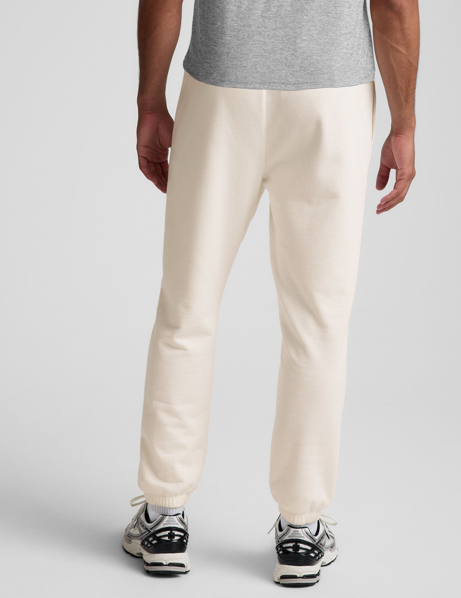man wearing a gray crew neck t-shirt and white fleece sweatpants on a plain background.