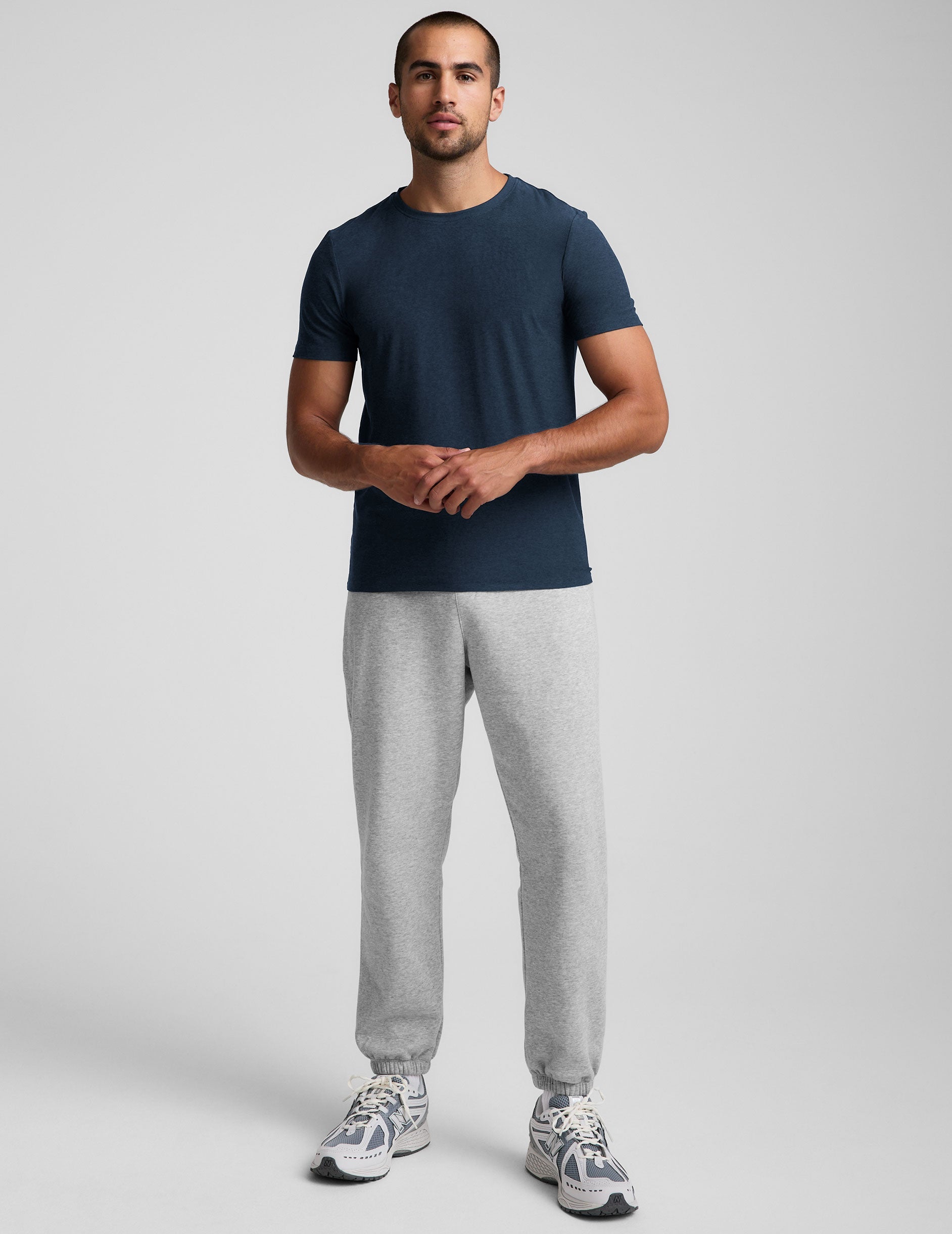 man wearing a navy crew neck t-shirt and gray fleece sweatpants on a light gray background.