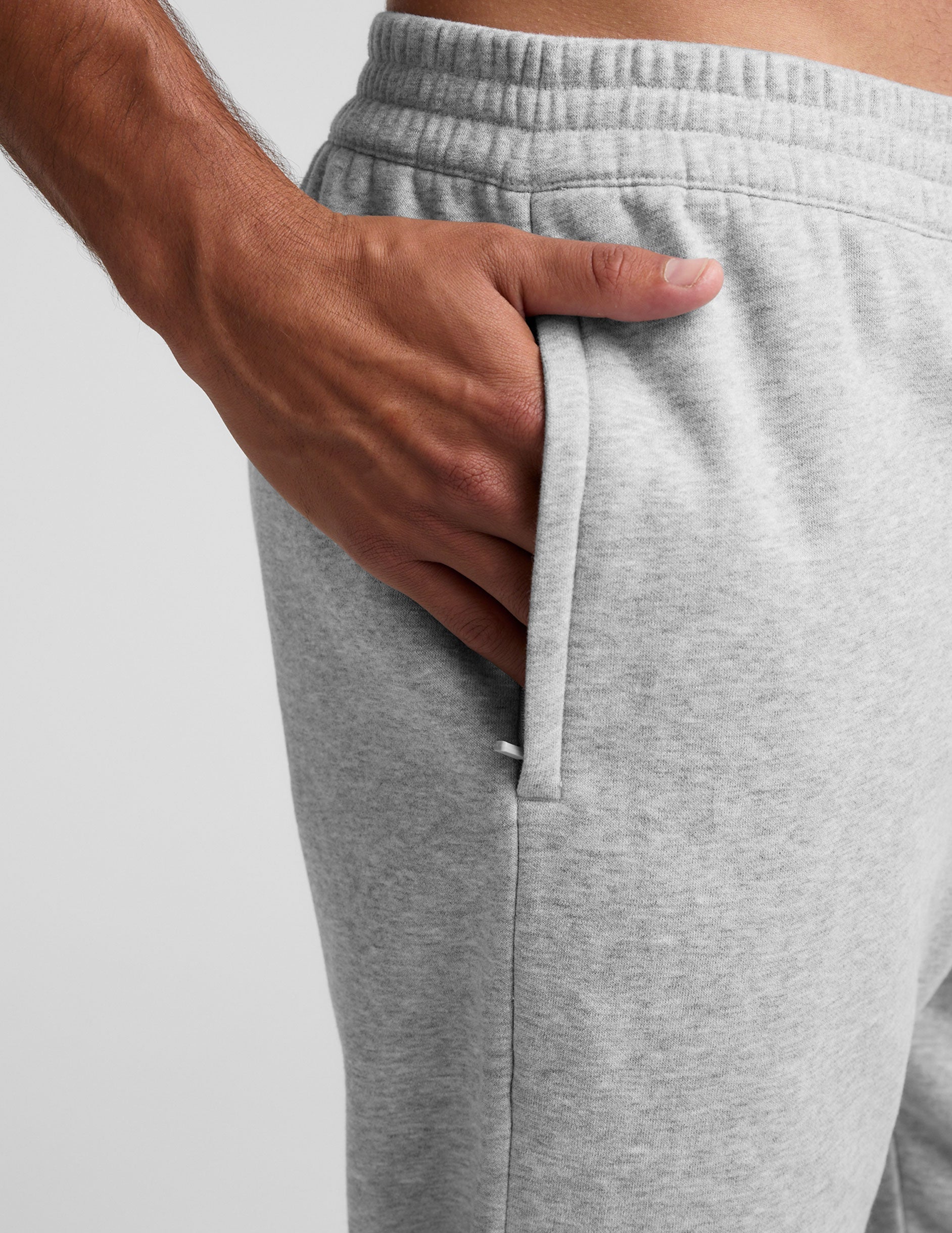 man wearing a black crew neck t-shirt and gray fleece sweatpants on a light gray background.