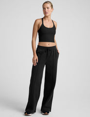 woman wearing a black cropped tank and fleece pinktuck pants on a plain background.