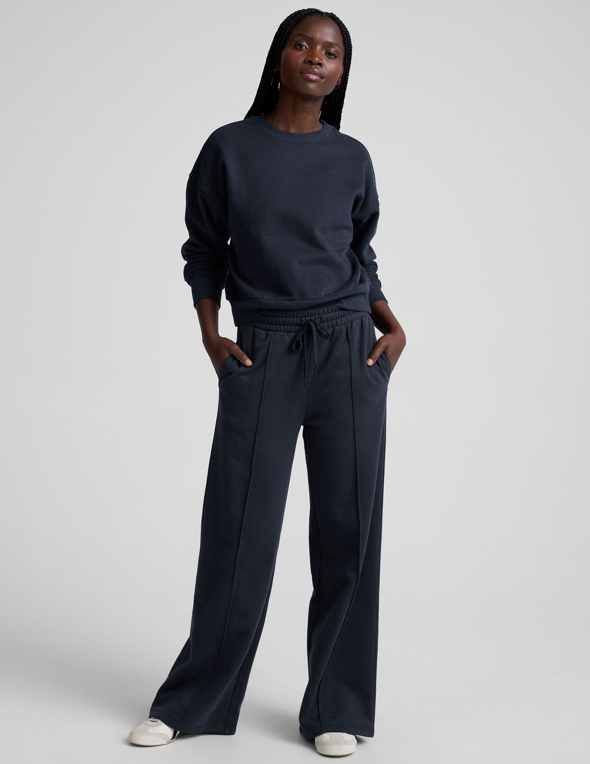 model is wearing a blue crewneck sweatshirt and blue fleece wide leg pants against a plain background.