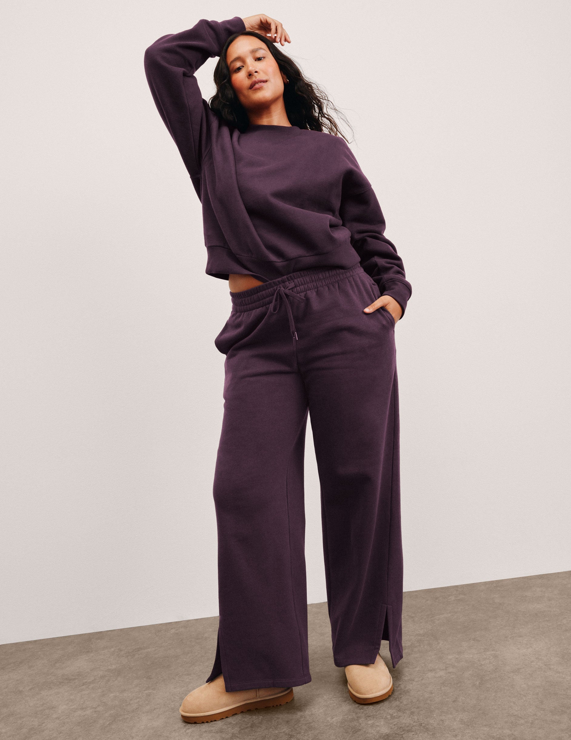 woman wearing a purple outfit with wide-leg pants on a plain background.