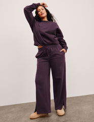 woman wearing a purple outfit with wide-leg pants on a plain background.