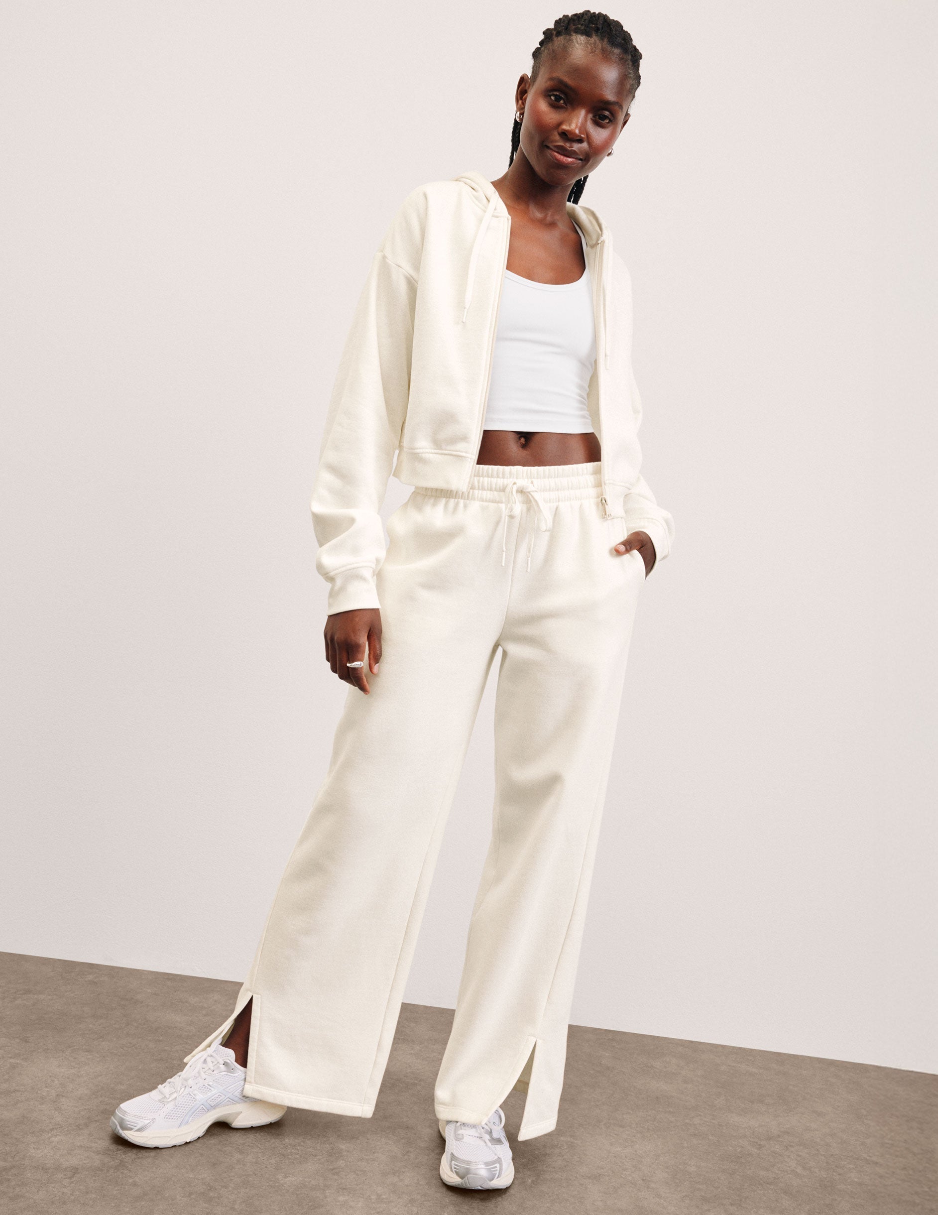 person wearing a white fleece zip-up jacket and white fleece wide leg pants with a plain background.