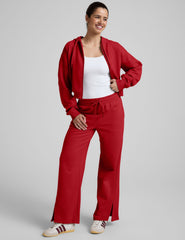 woman wearing a red fleece zip-up jacket and fleece pants with side slits against a plain background.
