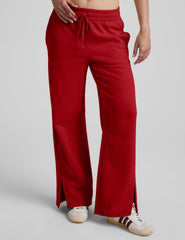 woman wearing a red fleece pants with side slits against a plain background.