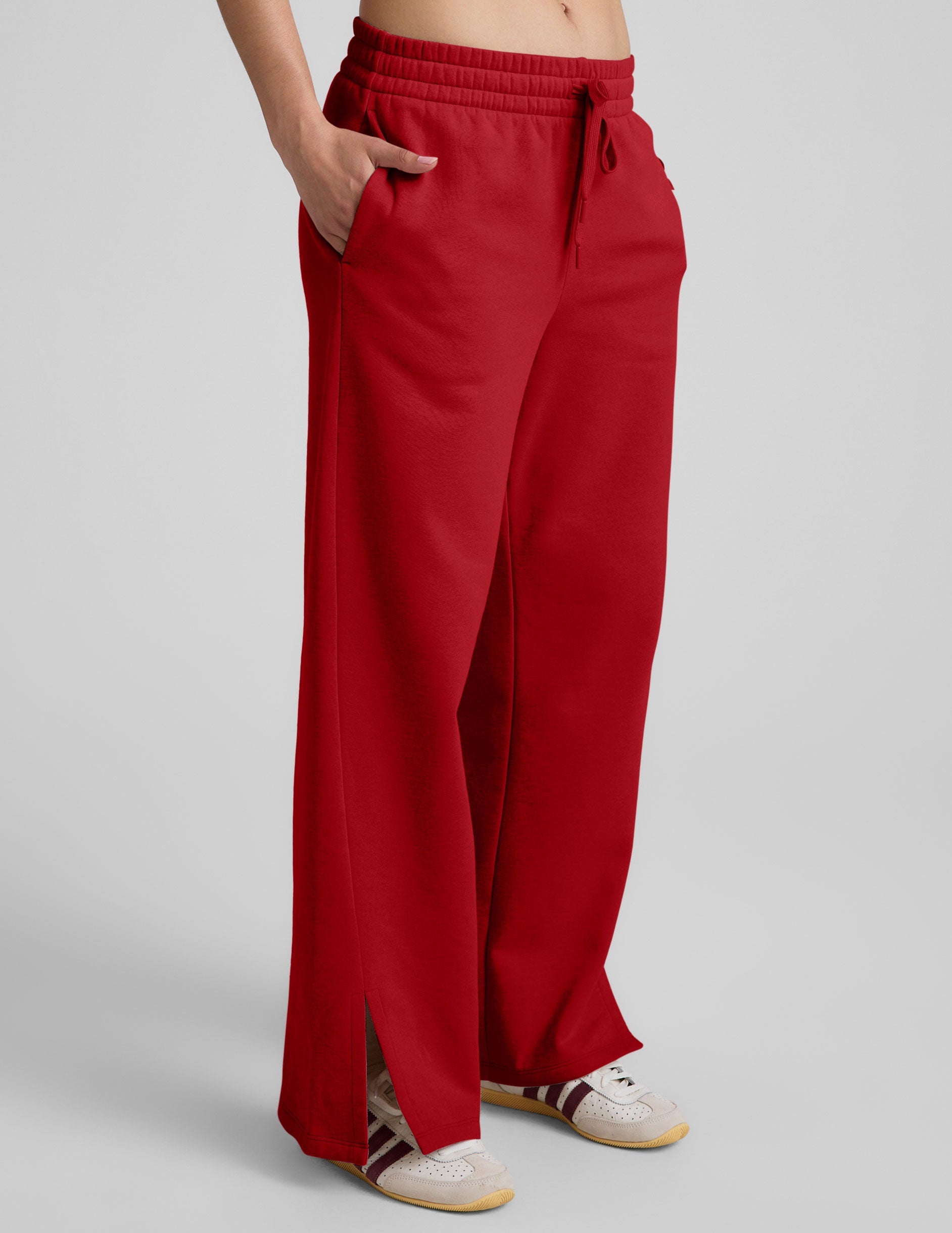 woman wearing a red fleece pants with side slits against a plain background.