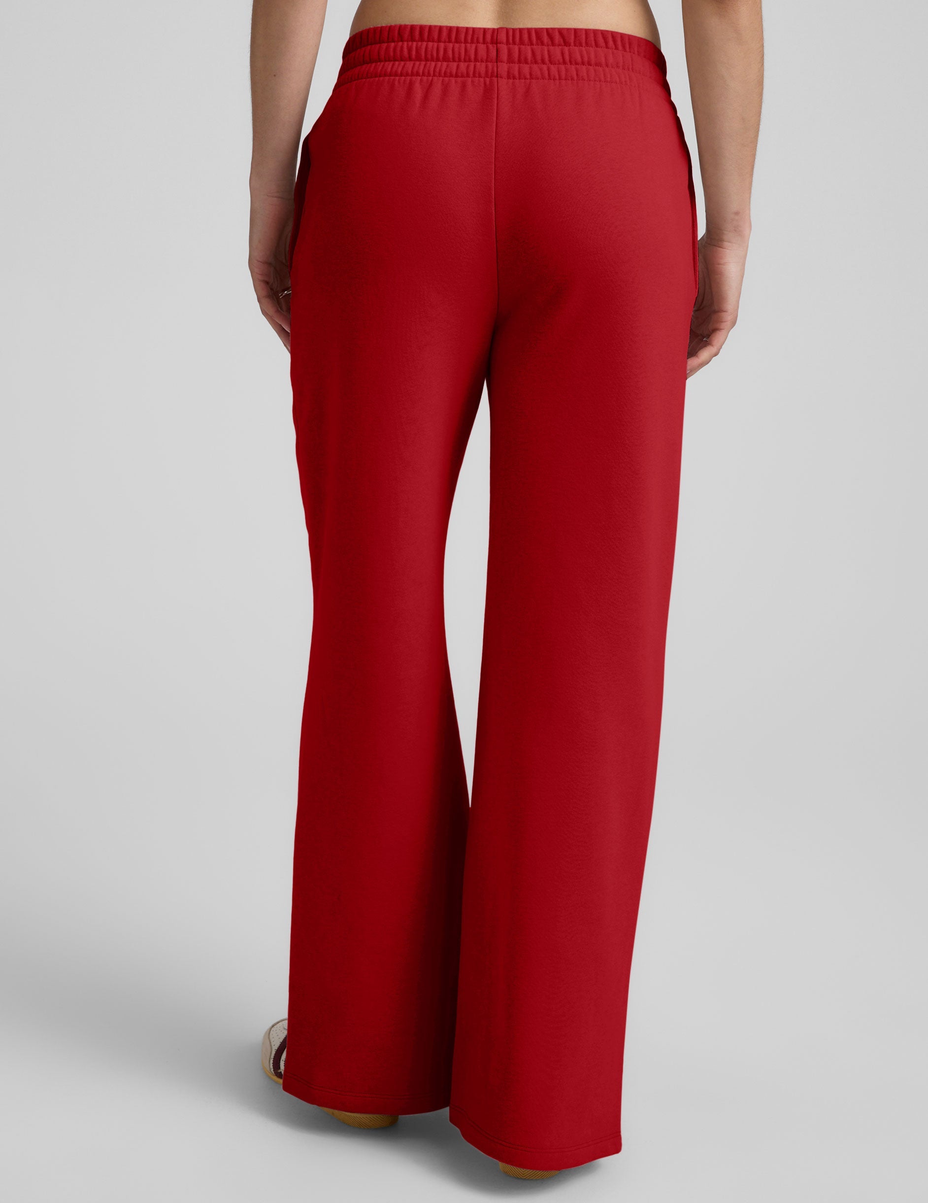 woman wearing a red fleece pants with side slits against a plain background.