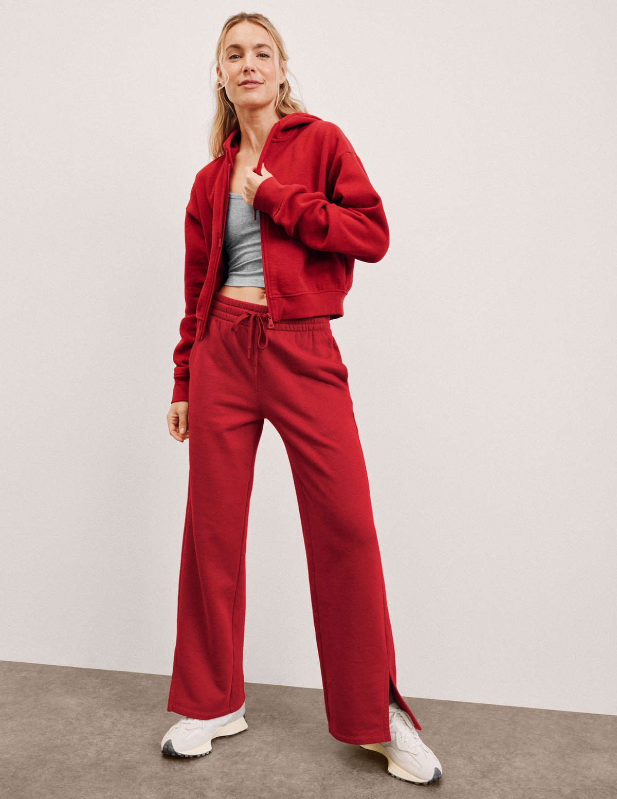 woman wearing a red fleece zip-up jacket and fleece pants with side slits against a plain background.