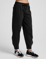 model is wearing black fleece barrel style sweatpants against a plain background.