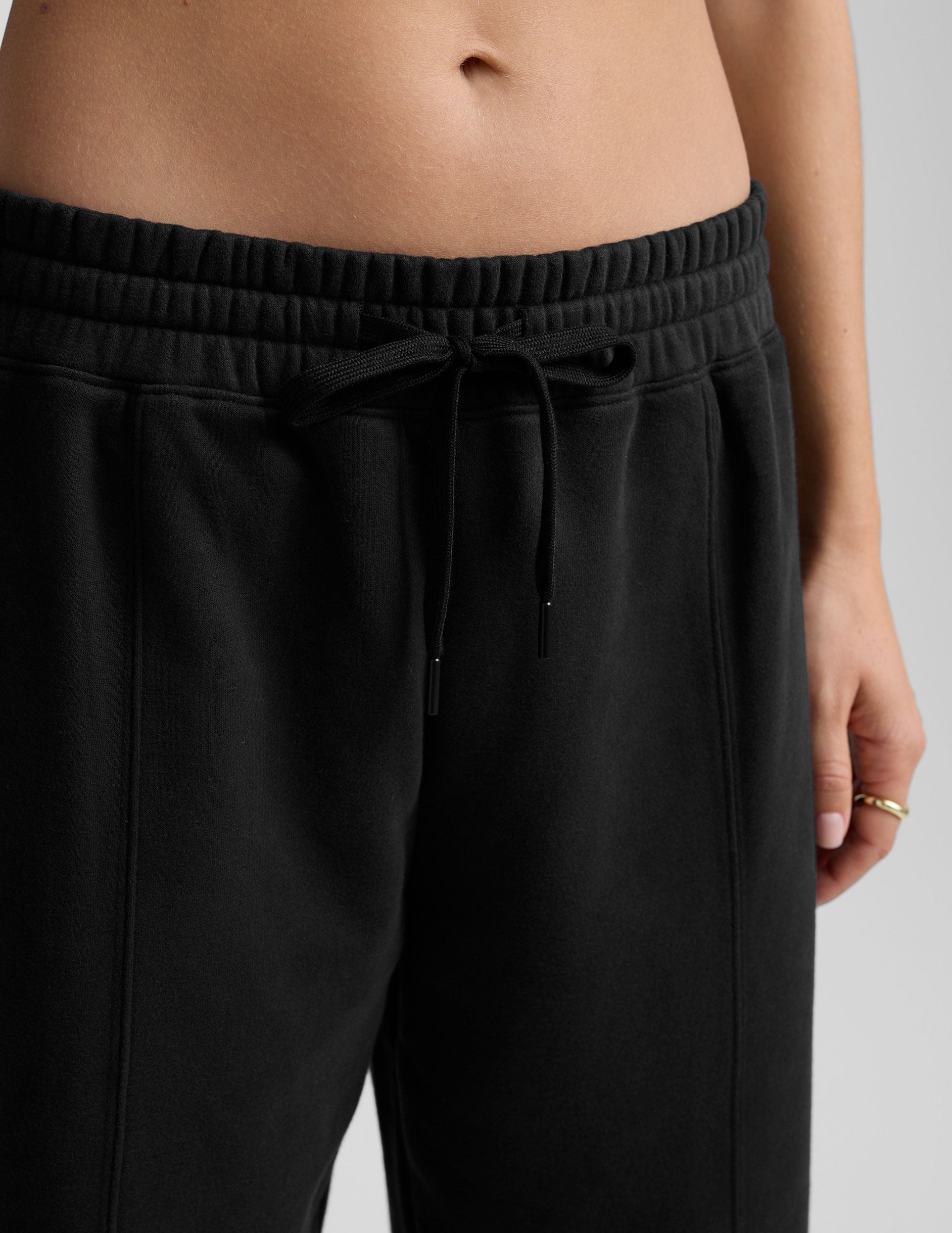 model is wearing black fleece barrel style sweatpants against a plain background.