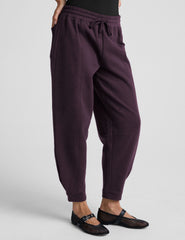 model is wearing purple fleece barrel style fleece sweatpants against a plain background.