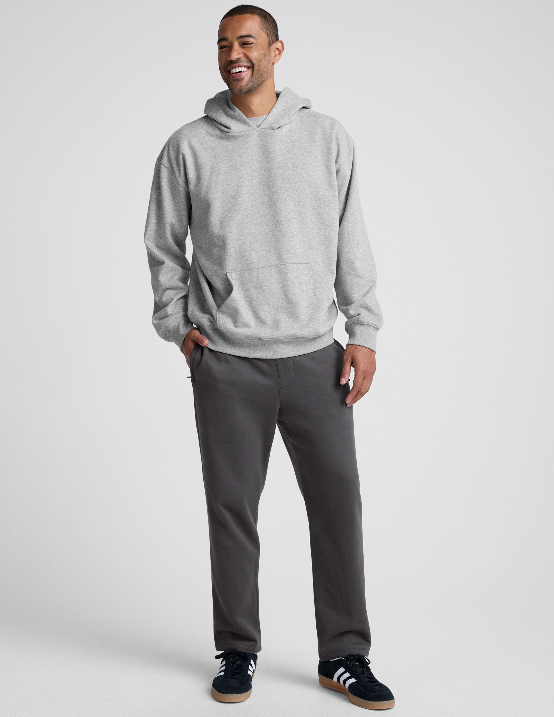man wearing a gray hoodie and gray straight leg sweatpants on a plain background.