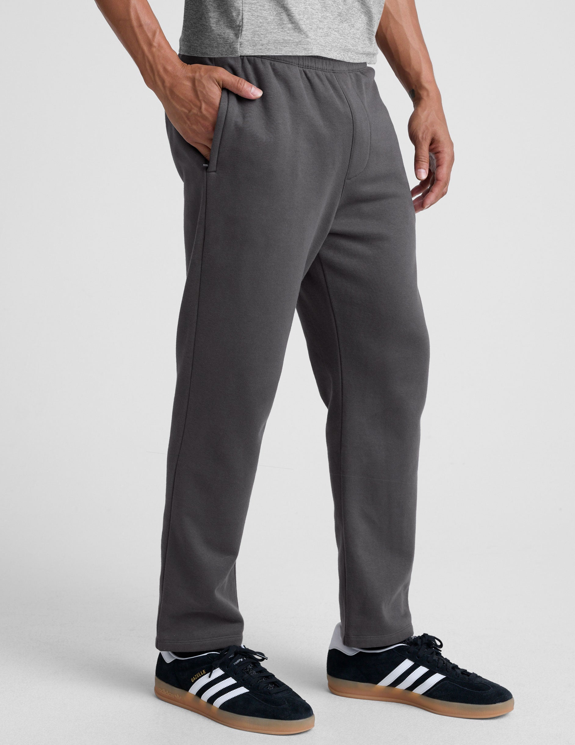 man wearing a gray shirt and gray straight leg sweatpants on a plain background.